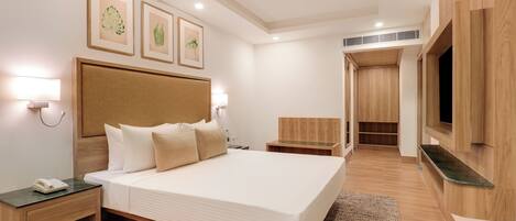 A modern hotel room with a large bed, bedside tables, a TV, and framed artwork on the wall.