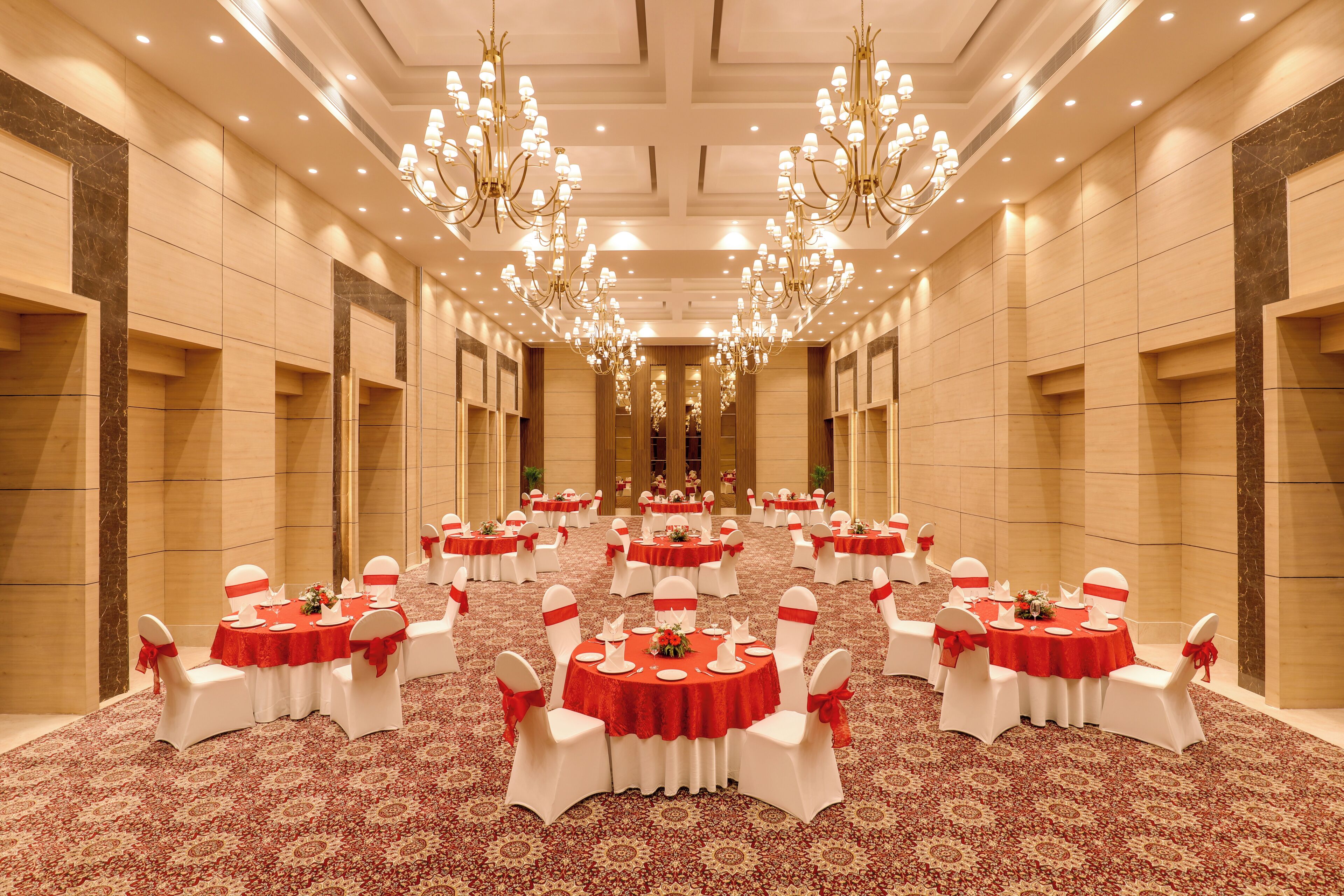 A banquet hall with multiple round tables, each with white chairs and red tablecloths, arranged in rows.