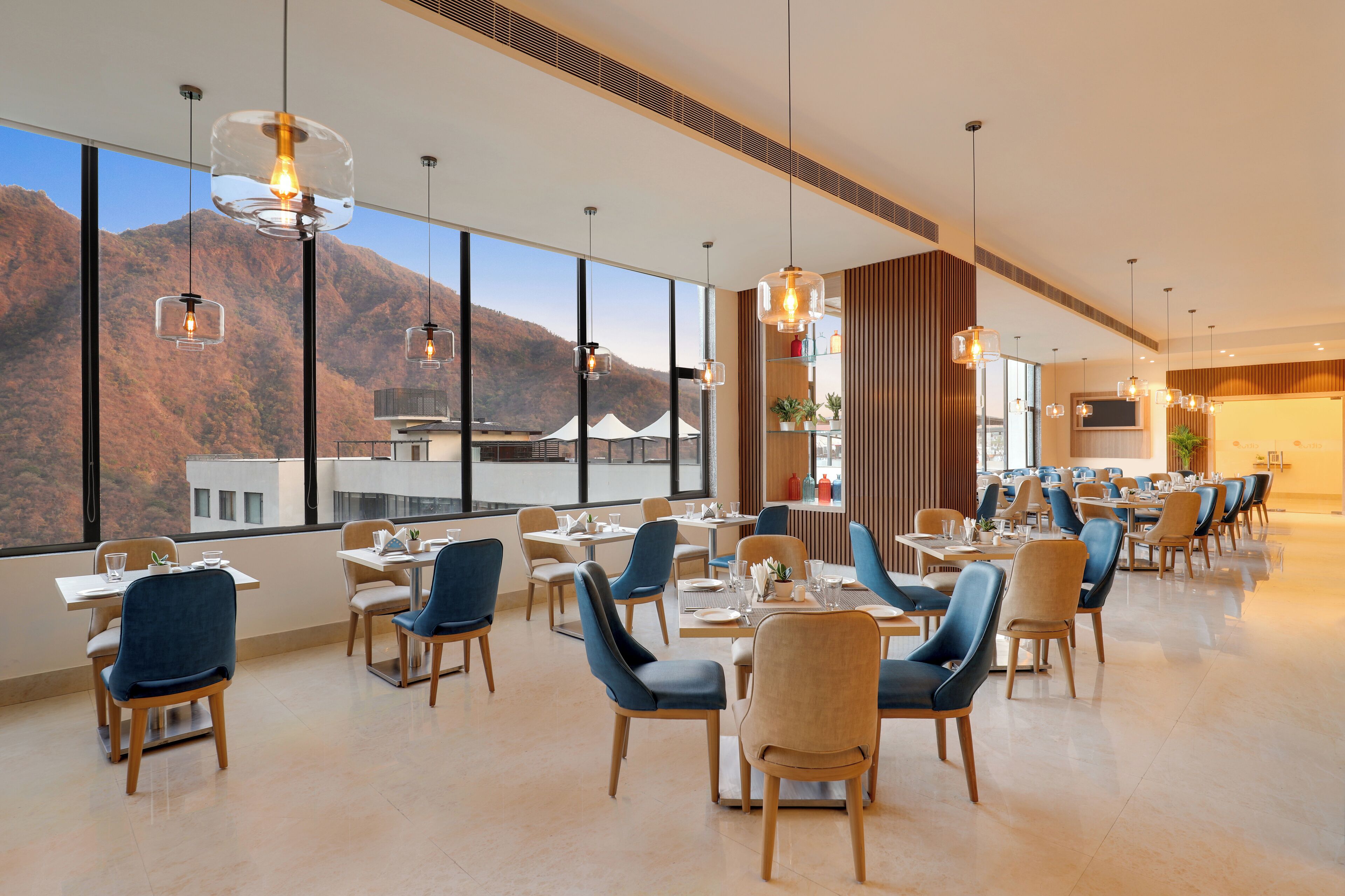 A modern dining area with tables and chairs, large windows with a mountain view, and pendant lighting.