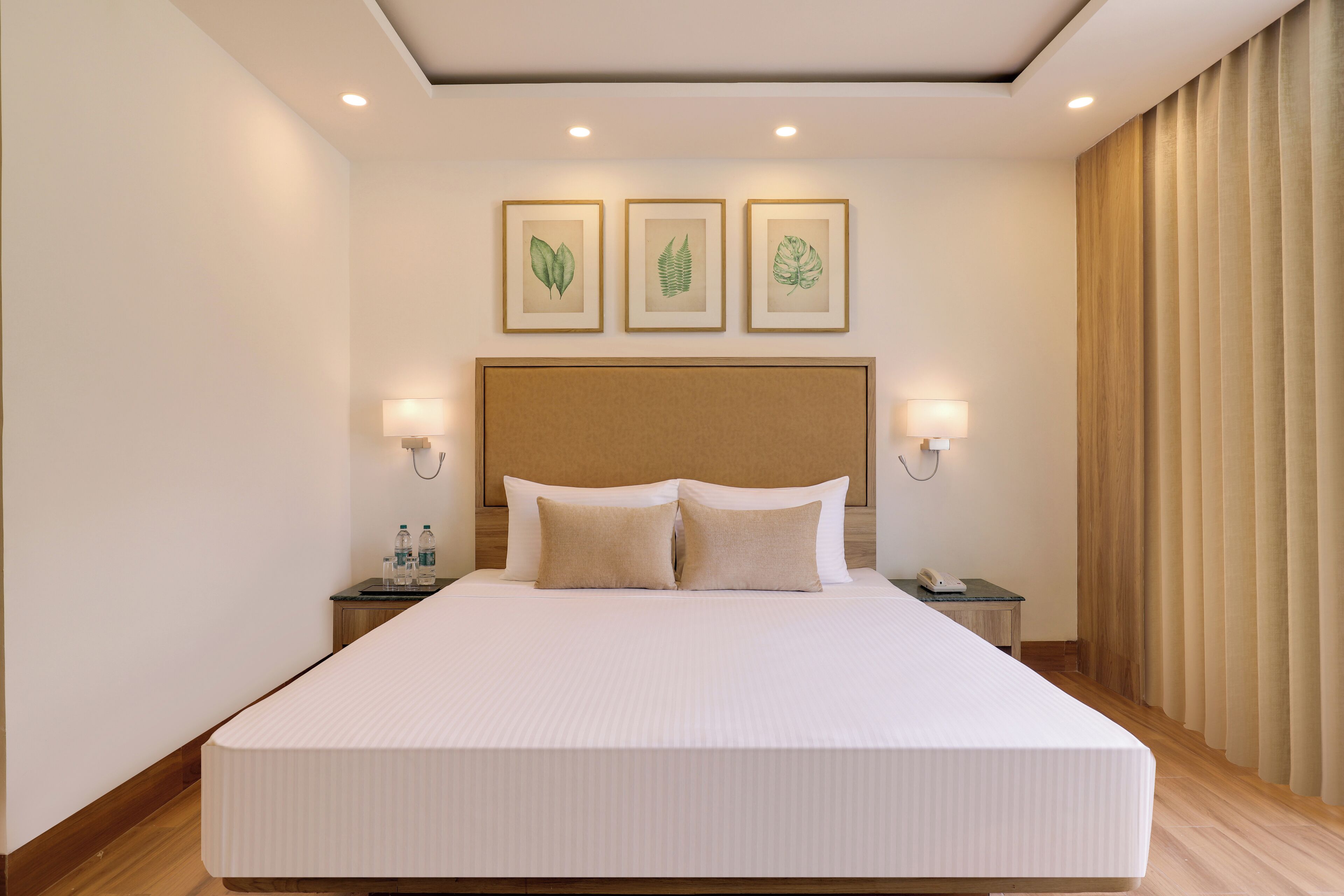 A large bed with a headboard, two bedside tables, and three framed botanical prints on the wall.