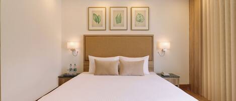 A large bed with a headboard, two bedside tables, and three framed botanical prints on the wall.
