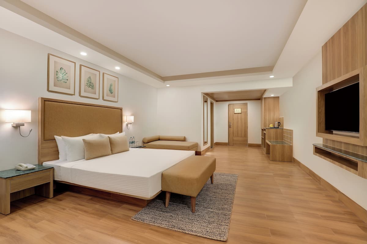 A modern hotel room with a large bed, bedside tables, a flat-screen TV, and a wooden wardrobe.