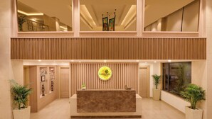 Zona de recepción de hotel con un mostrador de madera, un espejo grande y un cartel que dice 'Lemon Tree Hotel'.