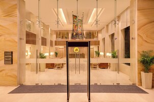 Un moderno vestíbulo de hotel con mostrador de recepción, puertas de vidrio y un candelabro central.