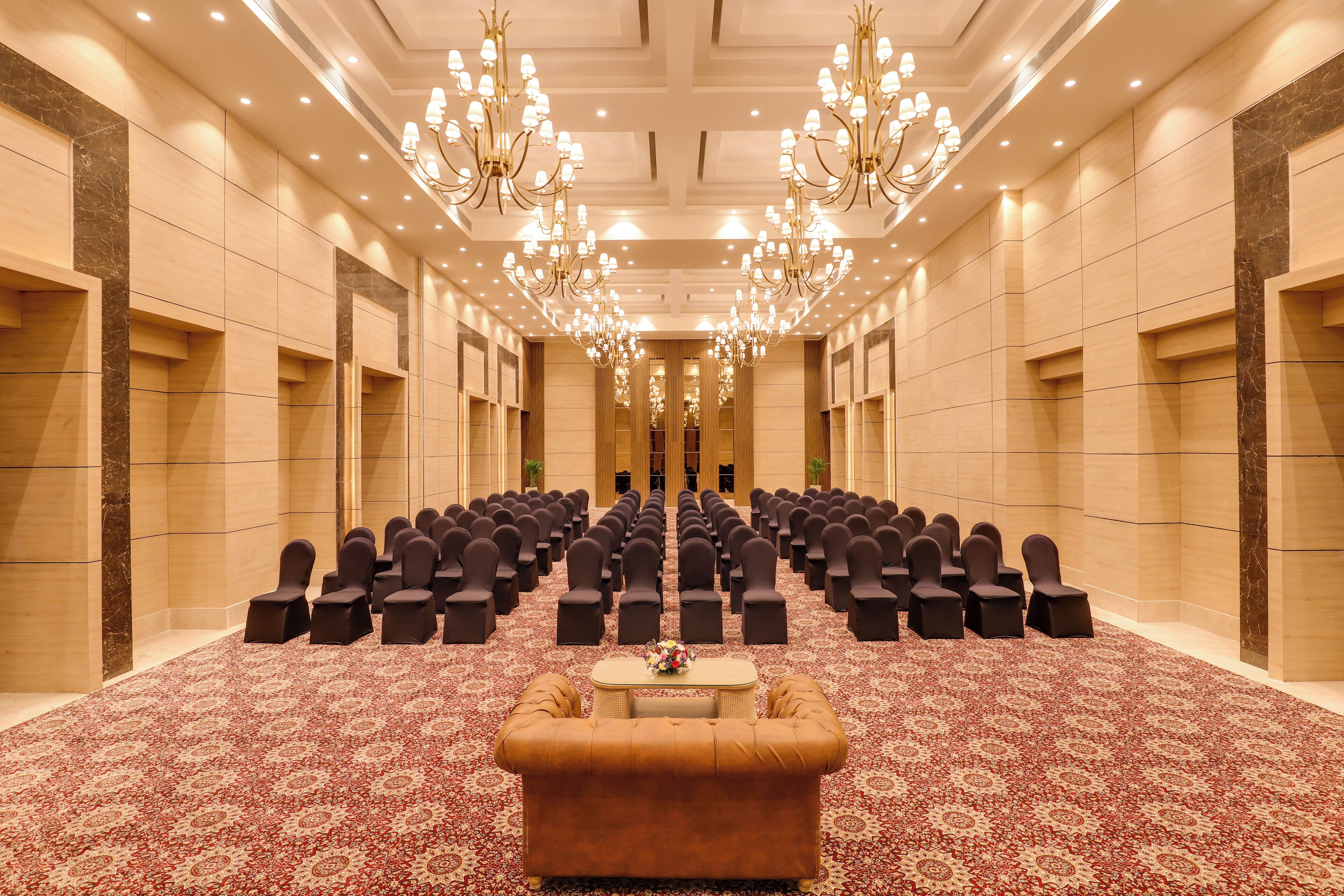 Un salón de conferencias con filas de sillas, un sofá central y candelabros.