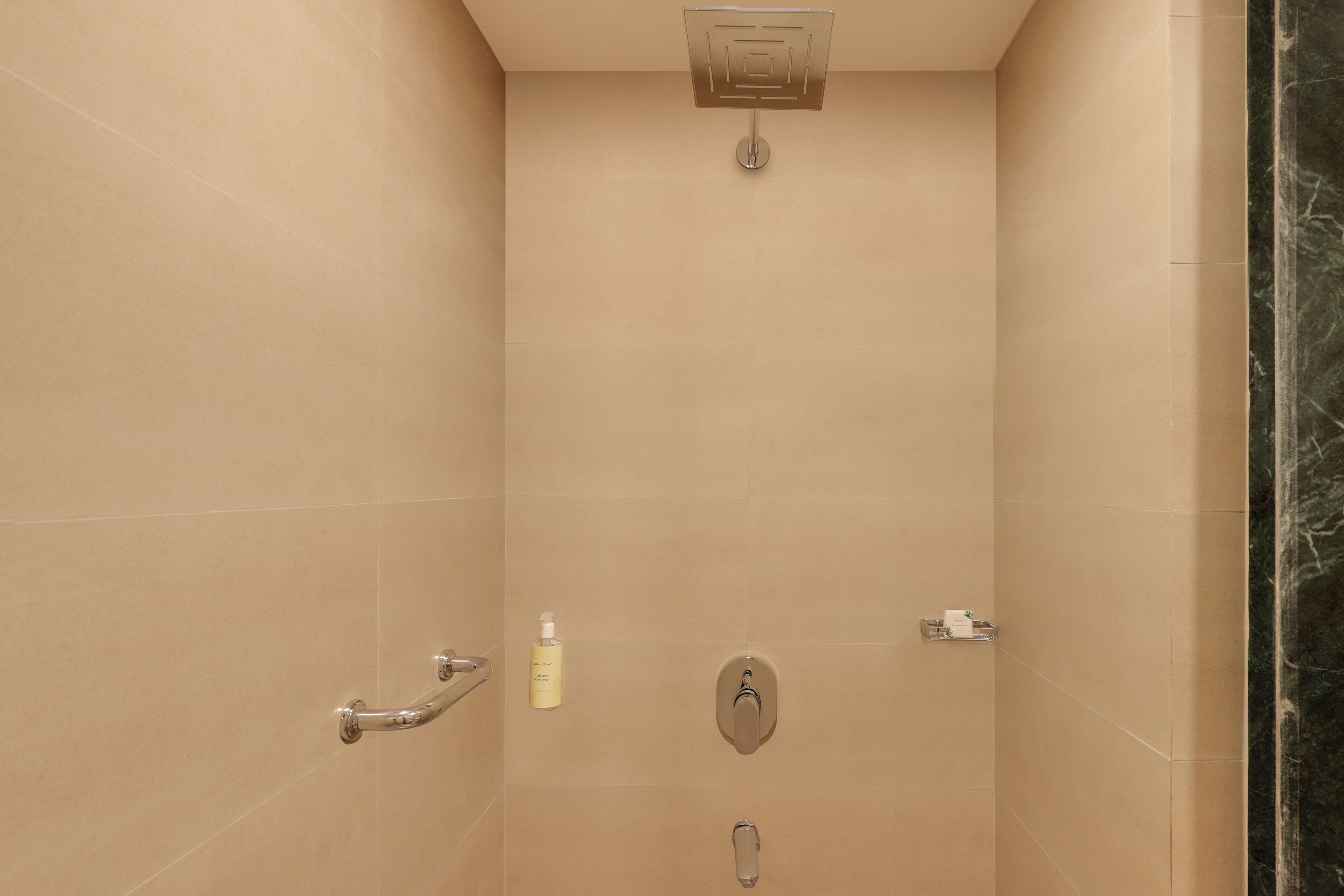 A shower with a handheld showerhead, a handheld showerhead, and a bottle of shampoo.