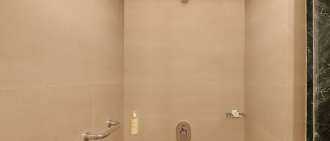 A shower with a handheld showerhead, a handheld showerhead, and a bottle of shampoo.