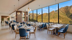 Un comedor amplio con mesas y sillas, ventanas grandes que ofrecen vistas a la montaña e iluminación colgante.