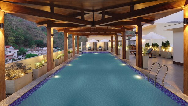 Una piscina con muelle de madera y sillones de descanso, rodeada de plantas en macetas y sombrillas.