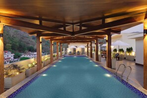 A swimming pool with a wooden deck and lounge chairs, surrounded by potted plants and umbrellas. - Lemon Tree Hotel, Rishikesh (Narendranagar)