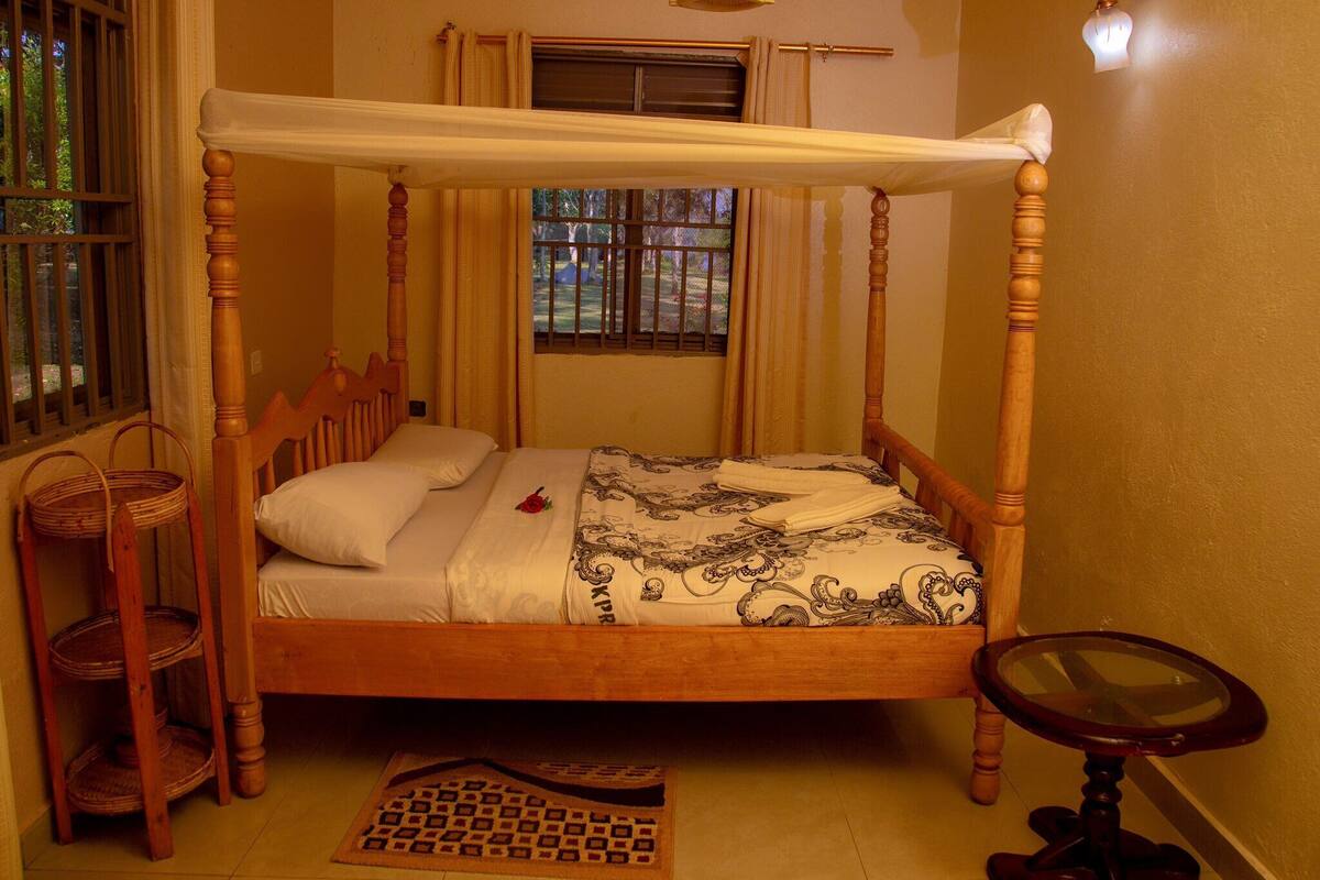 Een hemelbed met hemeltje, nachtkastje, raam met tralies en een houten stoel.