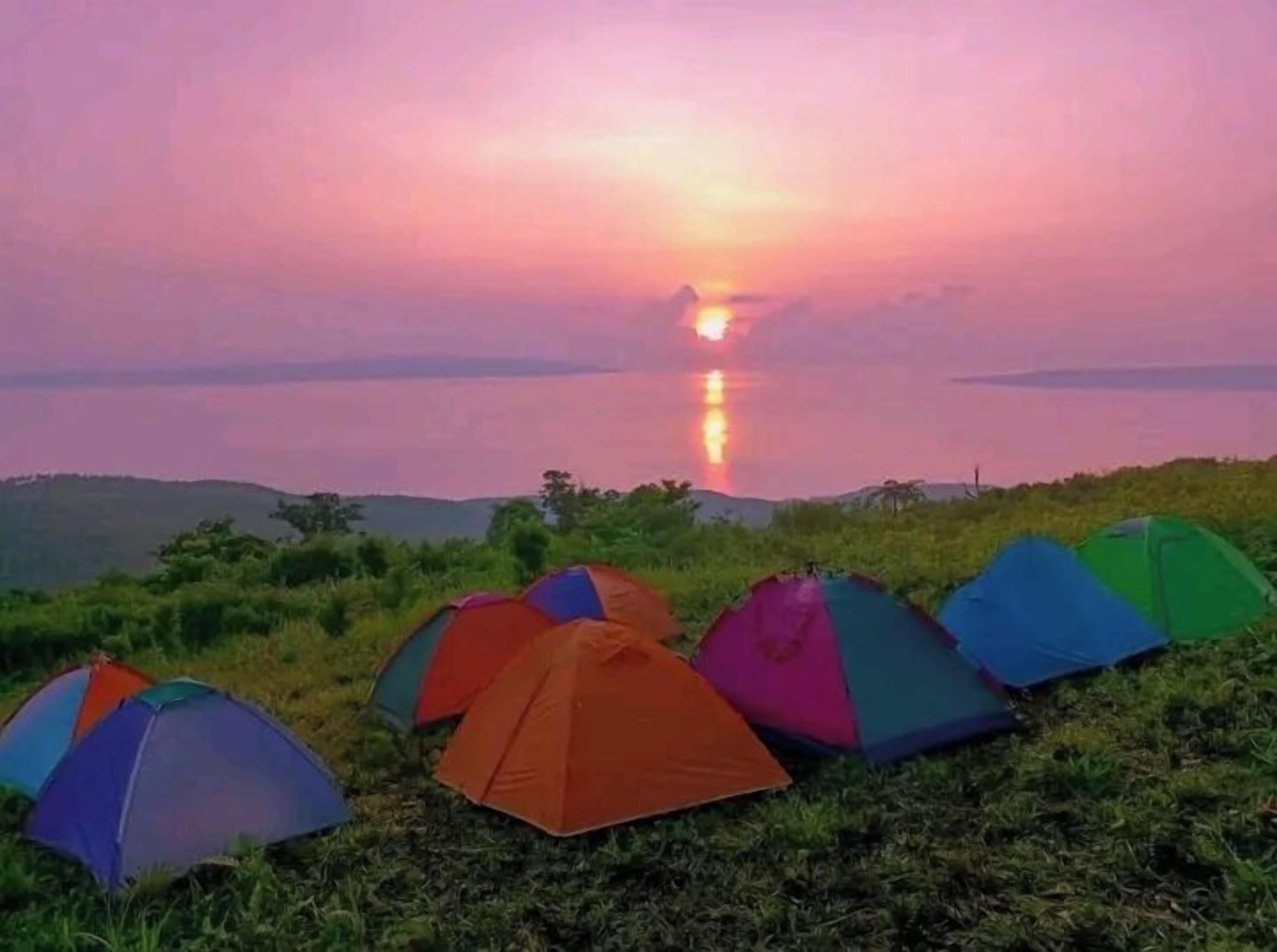 A sunset view with multiple colorful tents set up on grassy terrain.