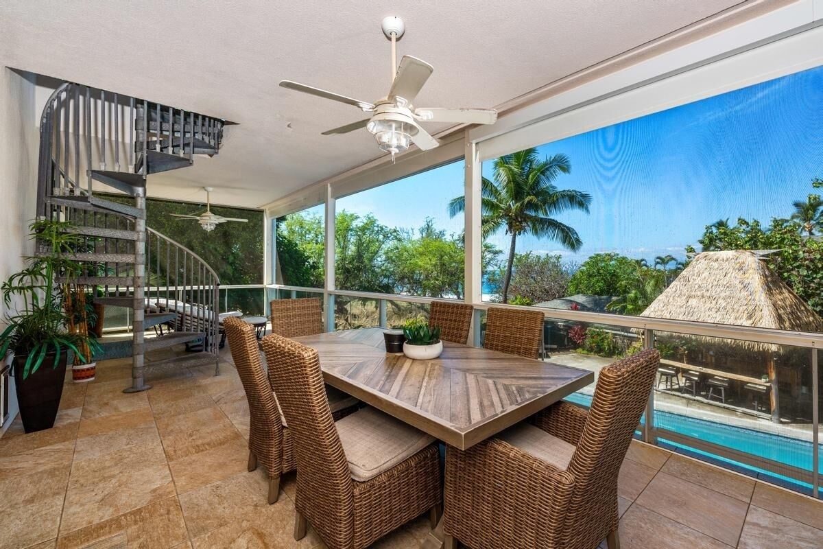 A spacious balcony with a dining table and wicker chairs, overlooking a swimming pool and lush greenery.