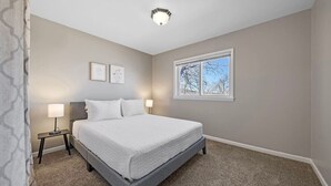 Een slaapkamer met een groot bed, twee nachtkastjes, een raam en een plafondlamp.