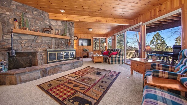 L’intérieur chaleureux d’un chalet avec une cheminée en pierre, un plafond en bois et une grande fenêtre donnant sur une terrasse.