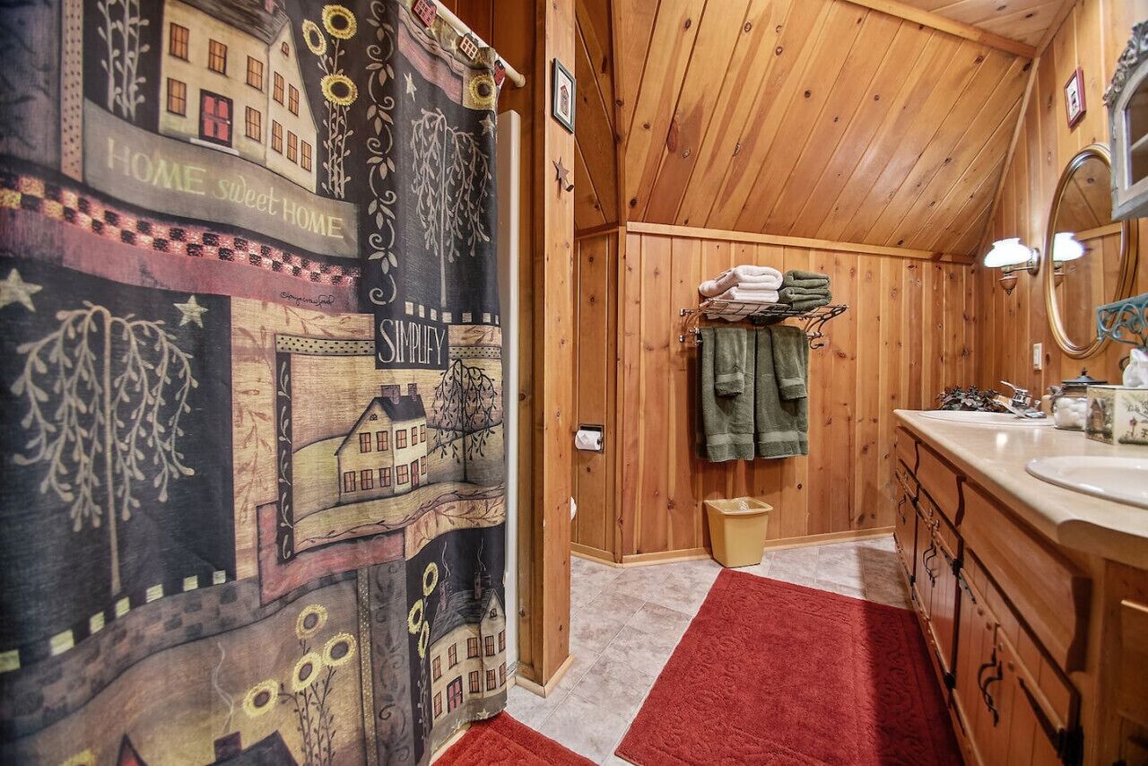 Ein Badezimmer einer Holzhütte mit einem roten Teppich, Holzschränken, einem Waschbecken und einem Spiegel.