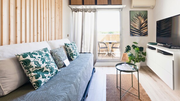Een moderne woonkamer met een bank, een kleine tafel, een televisie en een balkon met stoelen.