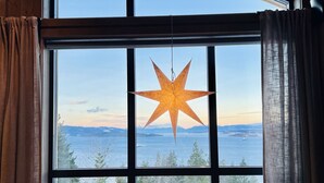 A room with a large window, a star-shaped hanging light, a chair, and a blanket on the windowsill.