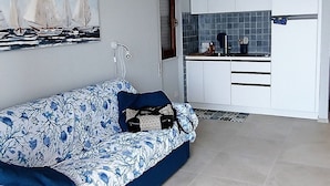 Ein Wohnzimmer mit einer Couch, einem Gemälde und einer Küchenzeile mit Schränken und einer Arbeitsfläche.