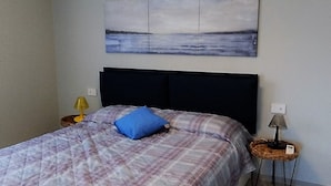 Ein Schlafzimmer mit einem Bett, einem Kopfteil, einem Wandbild, einer Nachttischlampe und einer Stehlampe.