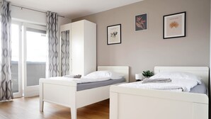 Une chambre avec deux lits simples, une armoire, une petite table de chevet avec une lampe et une fenêtre avec des rideaux.