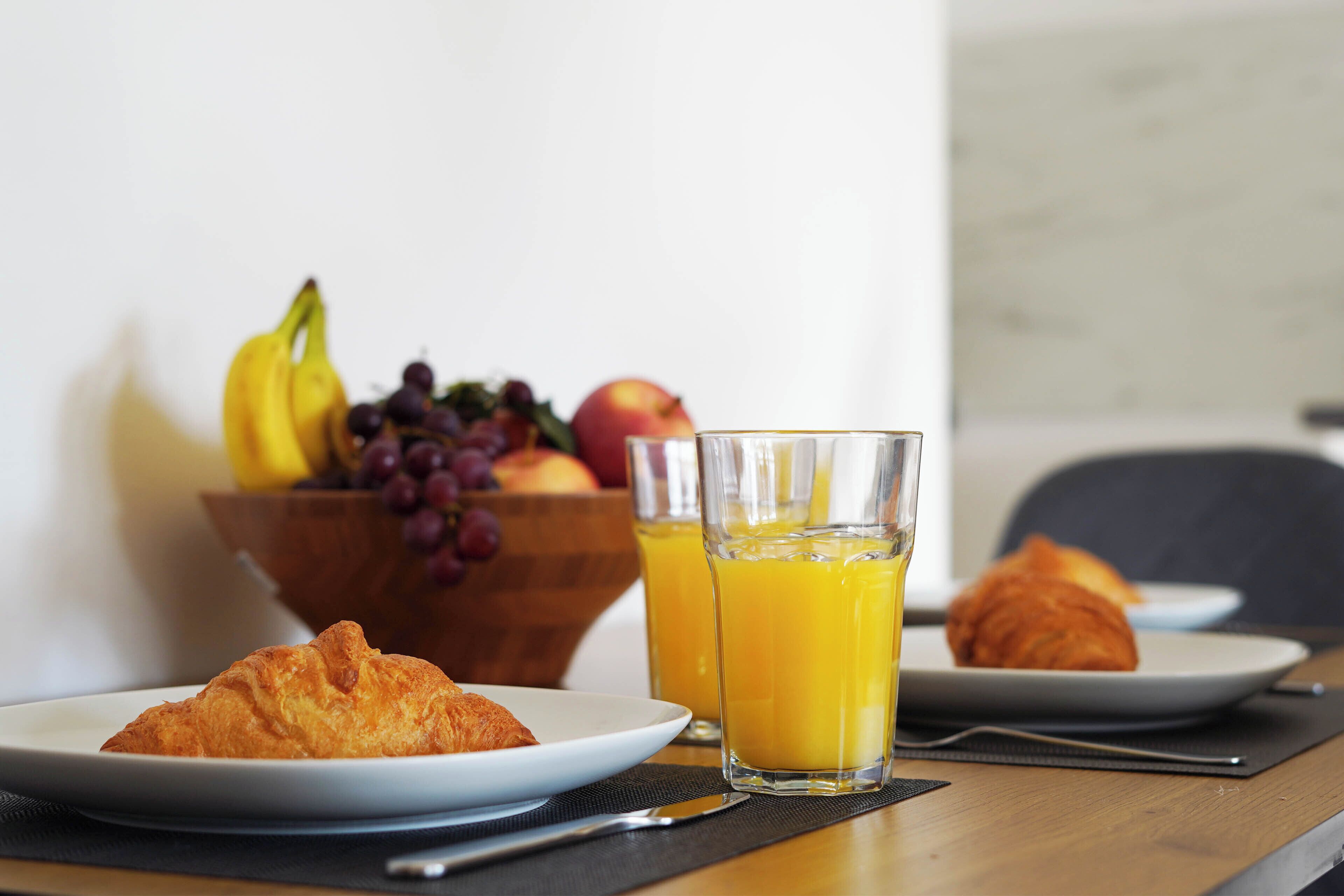 Ein Frühstückstisch mit Croissants, einer Obstschale und Gläsern Orangensaft.