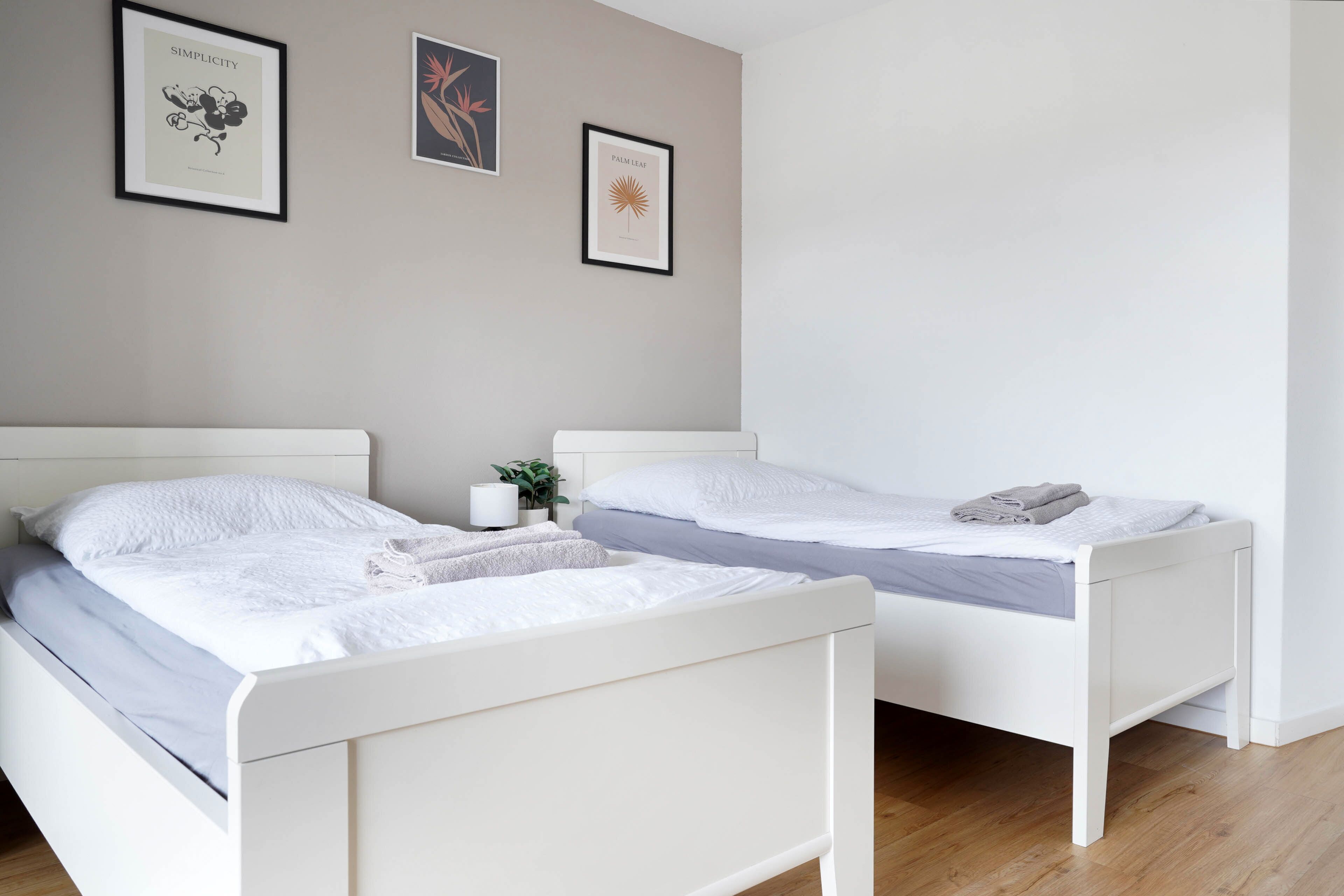 Ein Schlafzimmer mit zwei weißen Betten, einem Nachttisch mit Lampe und zwei gerahmten Bildern an der Wand.