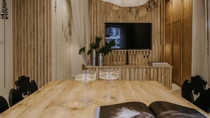 Une table à manger en bois, avec deux verres à vin, une plante en pot et un téléviseur, dans une pièce aux murs lambrissés.