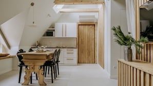 Une cuisine moderne avec des meubles en bois, une table à manger et des chaises. Le plafond est doté d’une structure en bois et une plante est posée sur une étagère.