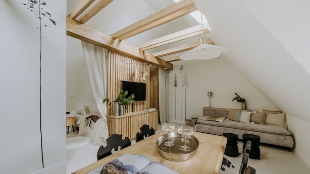 Une chambre à coucher confortable, aménagée en mezzanine avec un plafond en pente, une table à manger en bois sur laquelle est posé un magazine, un canapé et un téléviseur fixé sur un mur en panneaux de bois.
