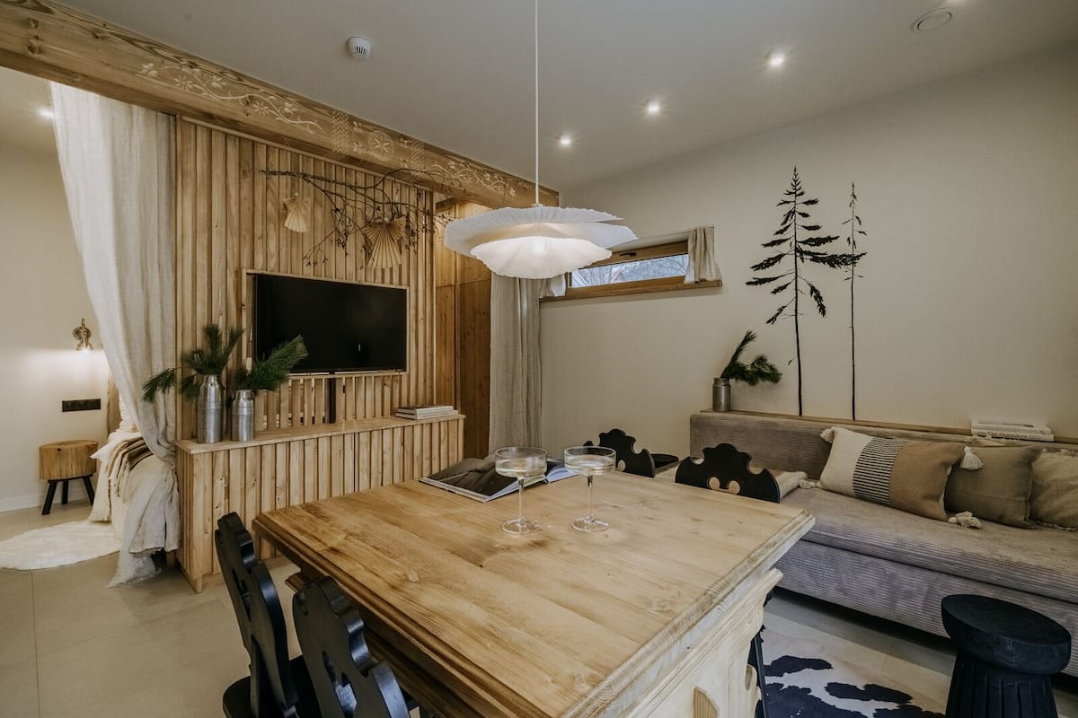 Una sala moderna con una mesa de comedor de madera, un sofá y un televisor fijado a una pared de madera.