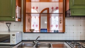 A kitchen with a double sink, a microwave, and a window with decorative curtains. - Da Procida 97 - Two Bedroom Apartment, Sleeps 5 (Procida)