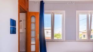 A room with a bed, a window with a curtain, a wooden door, and a view of buildings outside. - Da Procida 97 - Two Bedroom Apartment, Sleeps 5 (Procida)