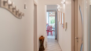 A hallway with a mannequin, a dining area with red chairs, and a door on the right. - Isba Da Procida - Two Bedroom Apartment, Sleeps 5 (Procida)