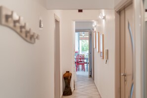 Un couloir avec un mannequin, un coin repas avec des chaises rouges et une porte sur la droite.
