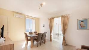 A dining area with a table and chairs, a TV on a wooden cabinet, and a window with curtains. - La Casa di Renata - Two Bedroom Apartment, Sleeps 5 (Procida)