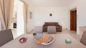 A modern living room with a sofa, a dining table with chairs, and a kitchen in the background. - La Casa di Renata - Two Bedroom Apartment, Sleeps 5 (Procida)