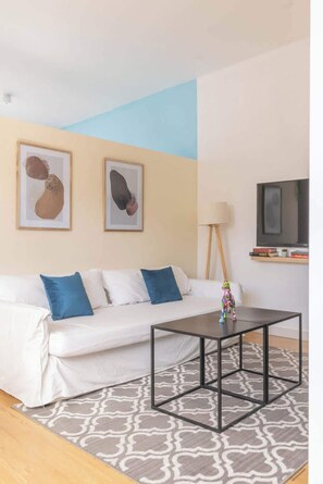 A modern living room with a white sofa, blue cushions, a black coffee table, and abstract art on the walls.