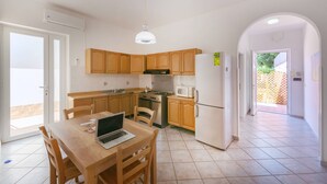 A modern kitchen with wooden cabinets, a gas stove, a microwave, and a refrigerator. There is a dining table with chairs and a laptop on it. - Pilòn 26 - Two Bedroom Apartment, Sleeps 5 (Procida)