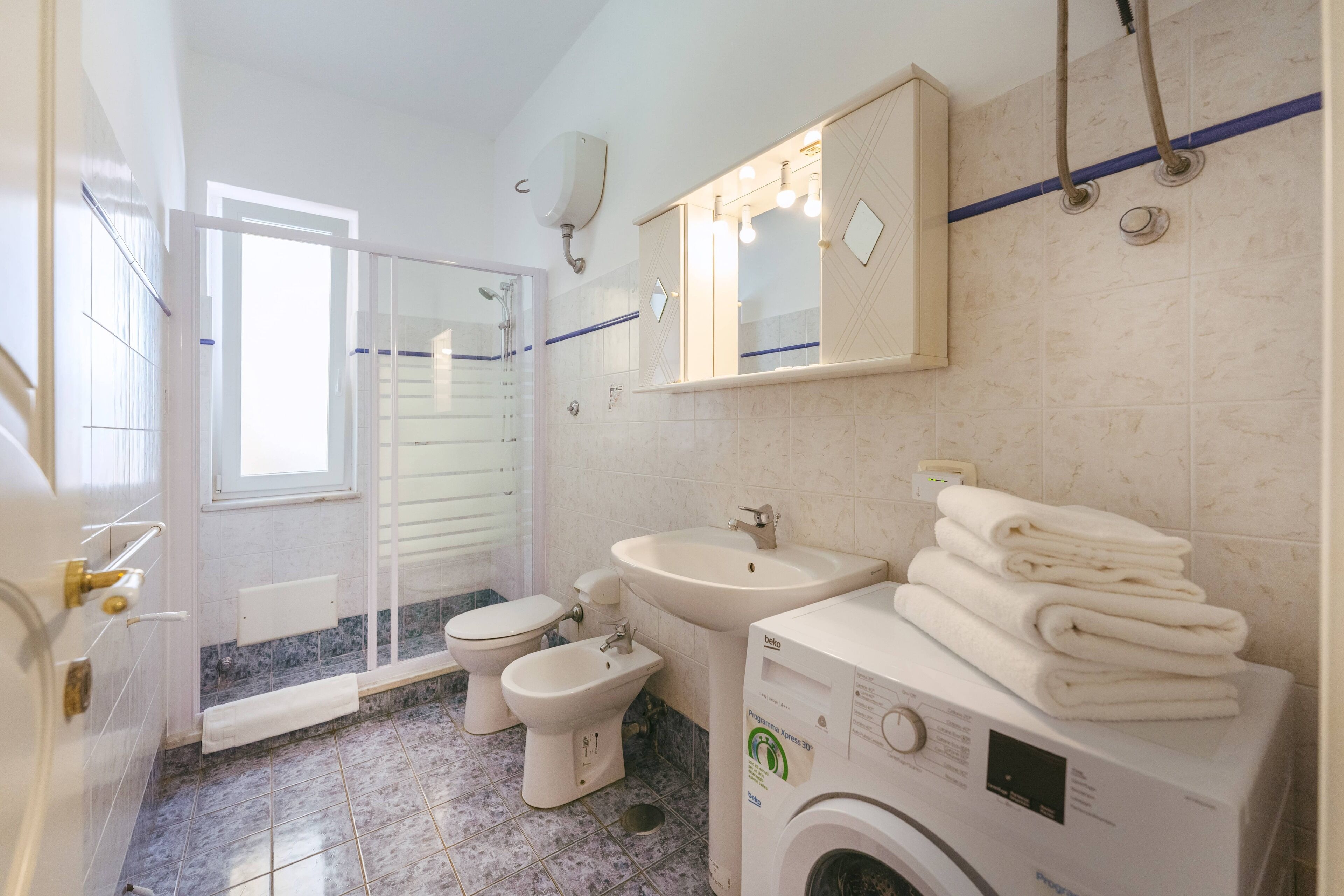 A bathroom with a toilet, bidet, sink, and a washing machine.