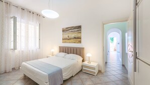 A bedroom with a bed, bedside tables, a painting, and a view of a hallway. - Pilòn 26 - Two Bedroom Apartment, Sleeps 5 (Procida)