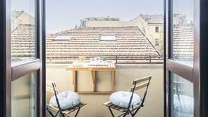 A balcony with a table and two chairs, overlooking a row of terracotta-tiled rooftops.