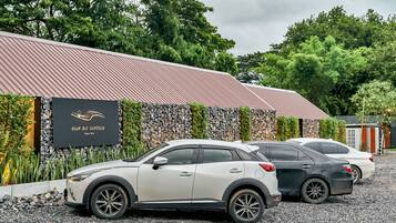 A parking area with three cars parked in front of a building with a stone wall and a sign that reads "BAAN RAI SANTISUK."