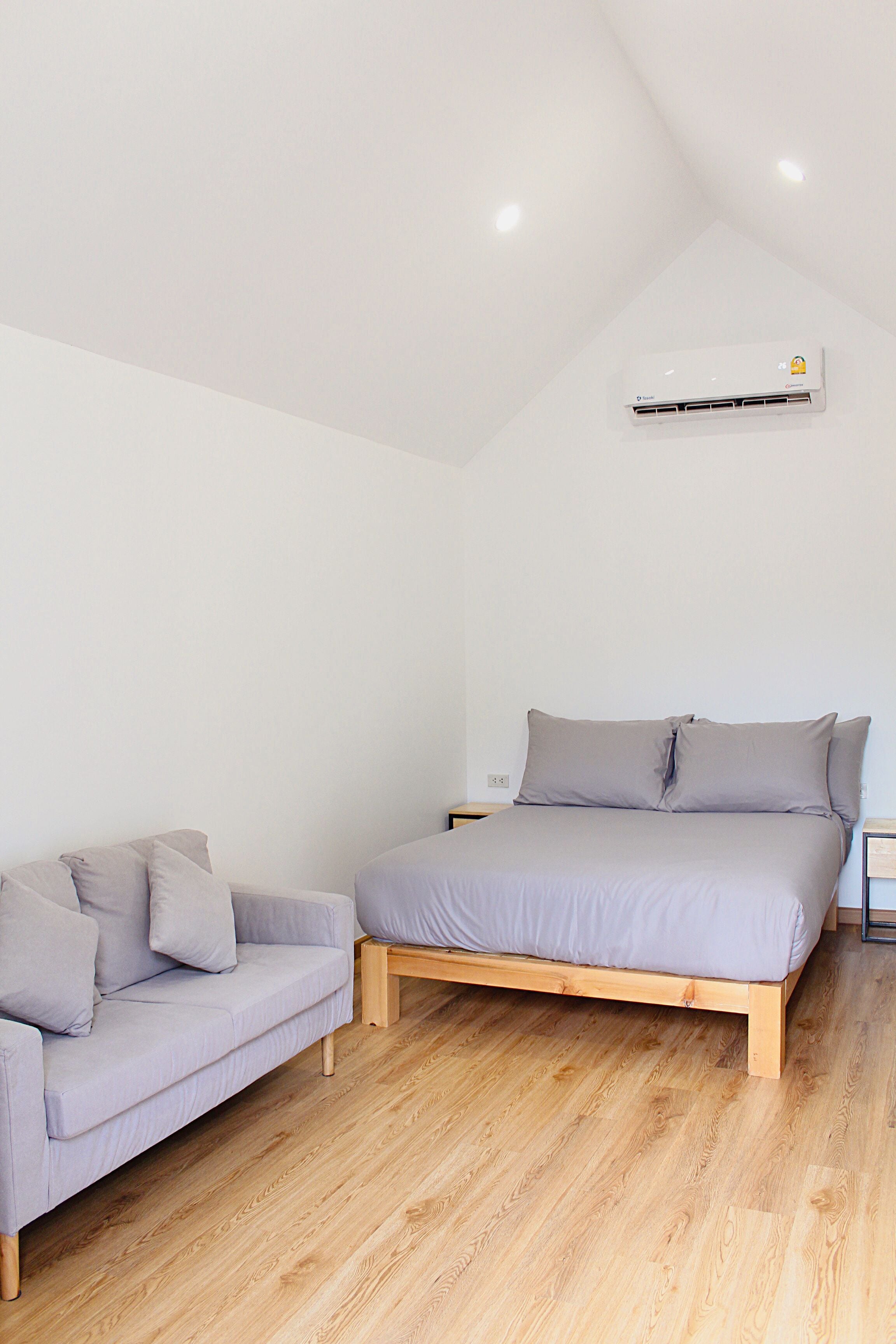 Ein Schlafzimmer mit einem Bett, einer Couch, Holzböden und einer Klimaanlage.