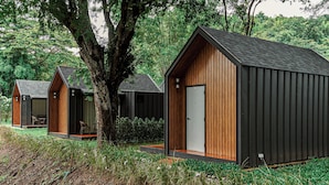 A row of modern cabins with wooden exteriors and black roofs, surrounded by lush greenery and trees. - Baan Rai Santisuk (Lom Sak)