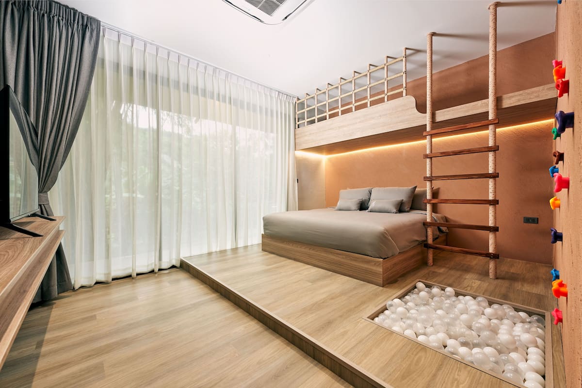 Un dormitorio moderno con una cama litera, una escalera de madera, un foso de pelotas y un ventanal con cortinas de gasa.