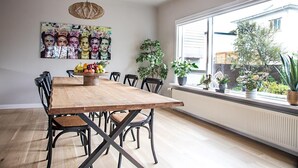 A dining area with a wooden table, black chairs, a fruit bowl, and a large window with plants on the sill. - Luxurious Villa in Reykjavik (Reykjavík)