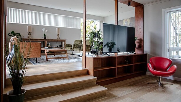 A modern living room with a wooden staircase, a flat-screen TV, a red chair, and a dining area with a table and chairs. - Luxurious Villa in Reykjavik (Reykjavík)
