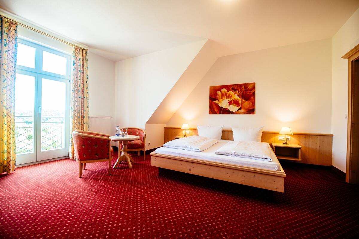 A hotel room with a large bed, a small table, a chair, and a painting on the wall.