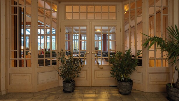 Entrada de un restaurante con puertas dobles, plantas en macetas y suelo de baldosas.